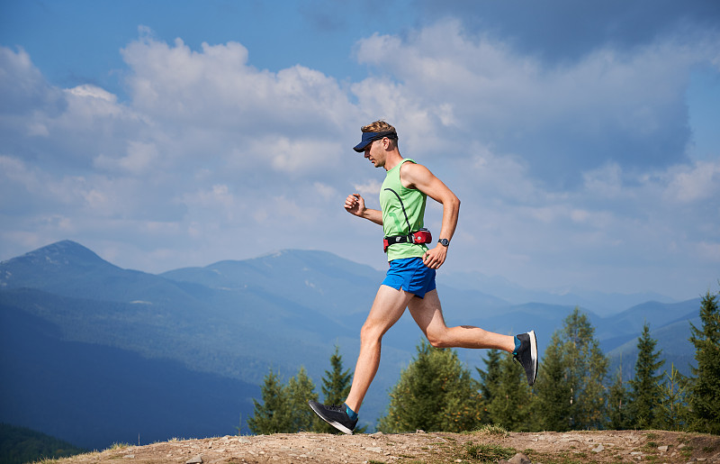 Trail runner in neon green activewear sprinting across mountain trail, breathable moisture-wicking sports fabric in action