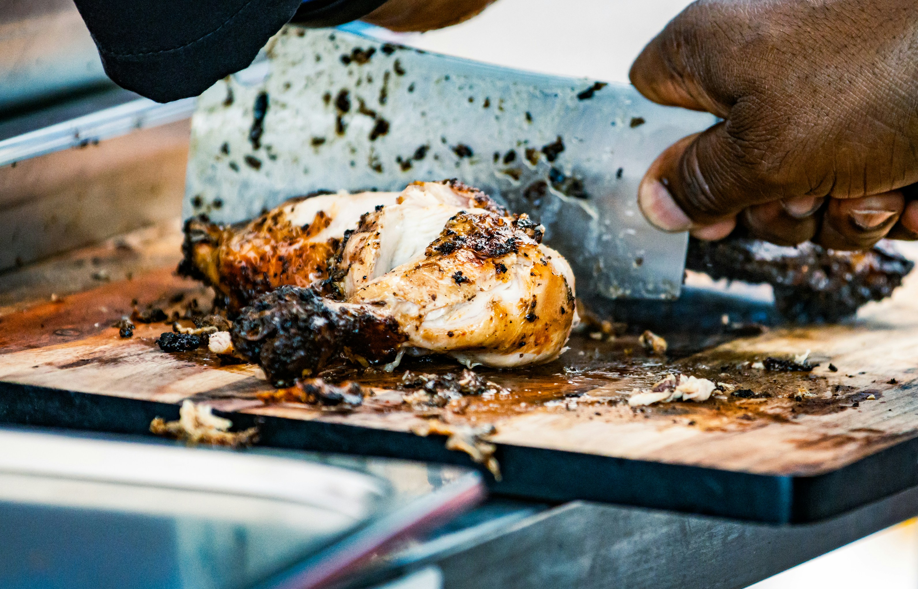 using stainless steel and wood cutting boards A person using a stainless steel cutting board to prepare raw chicken next to a wooden board with chopped vegetables