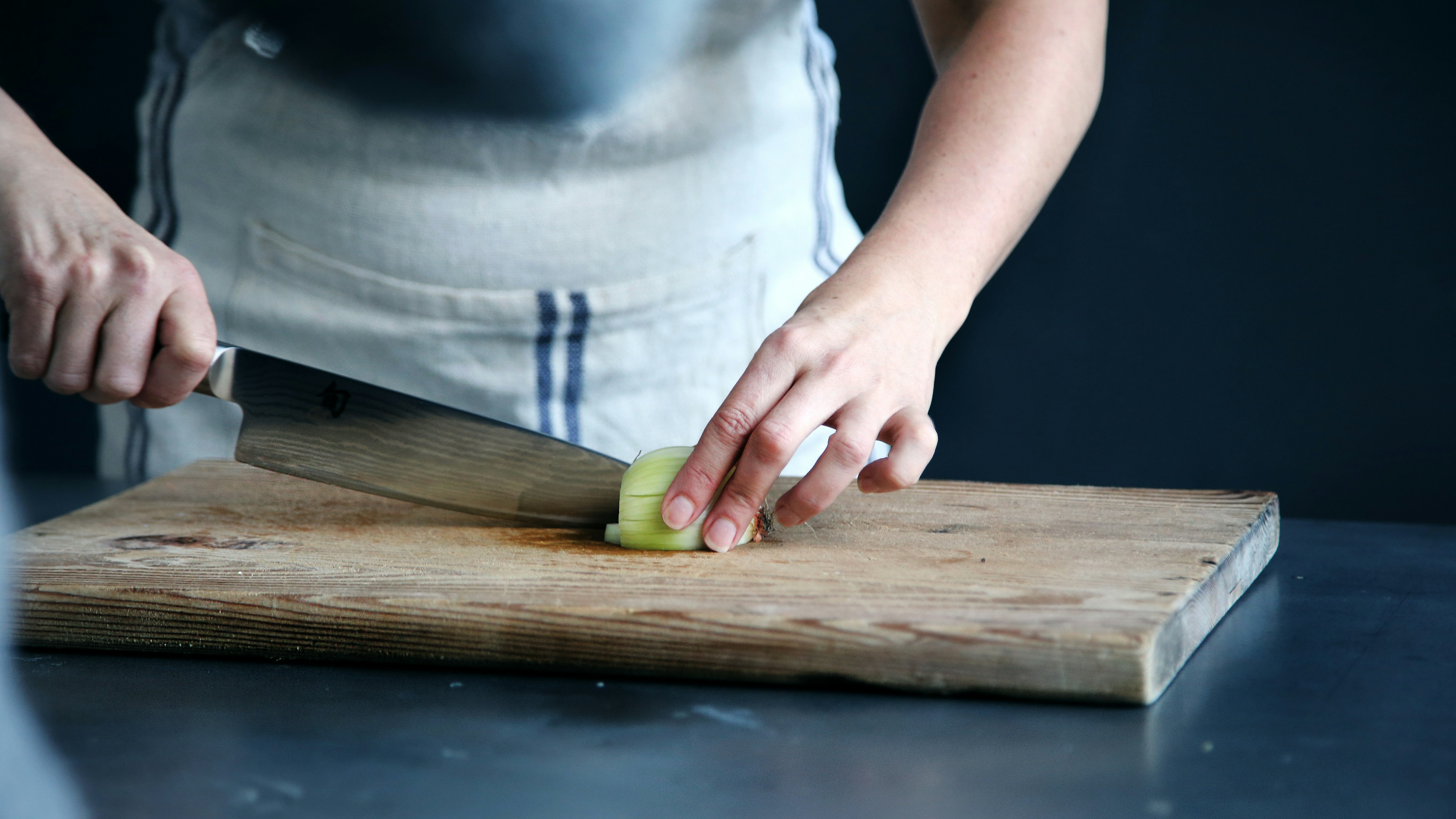 chopping vegetables on a wooden cutting board A person chopping vegetables on a large wooden cutting board in a well-lit kitchen