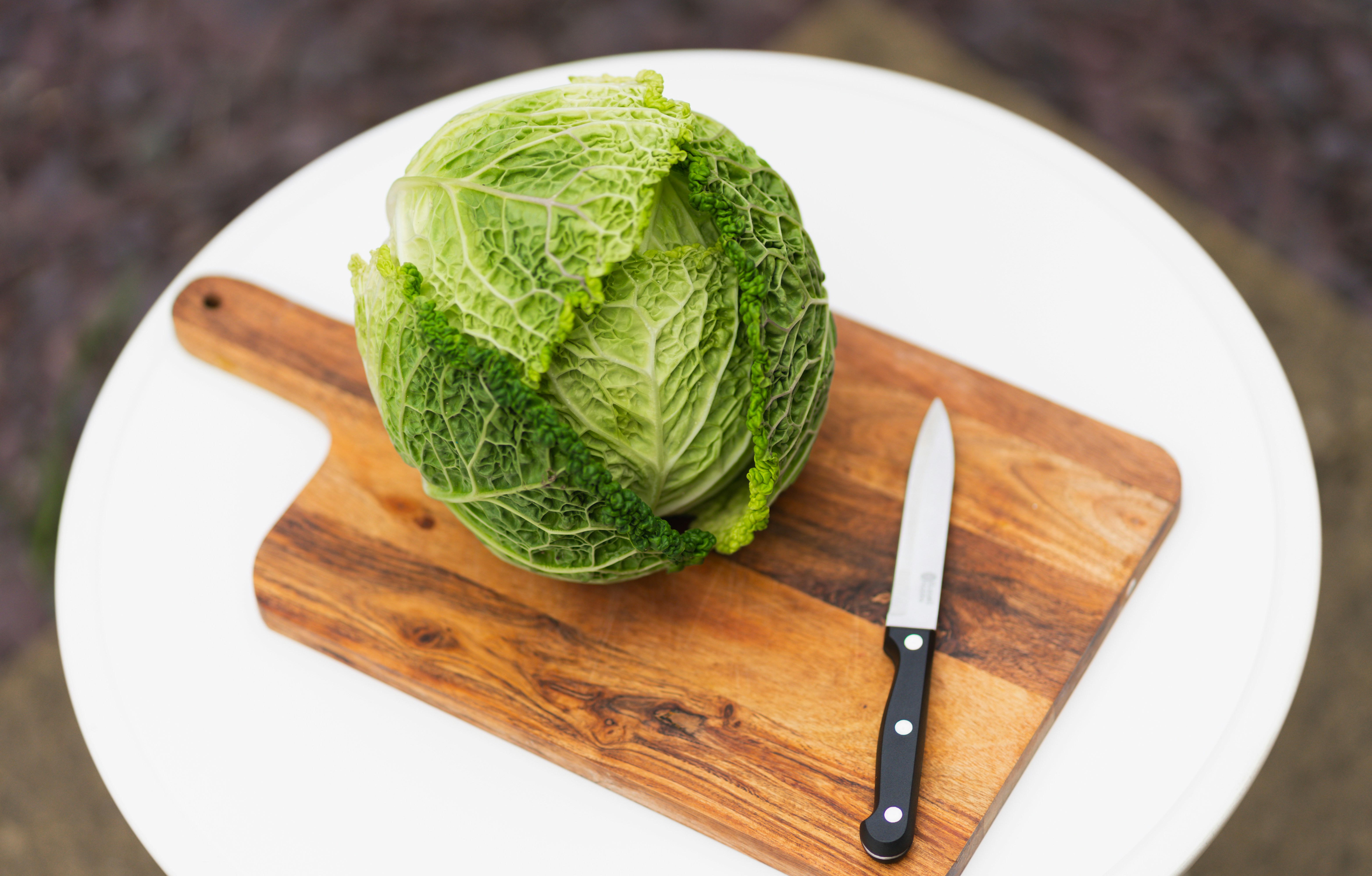 A person chopping a large head of cabbage on a large plastic cutting board for fermentation.