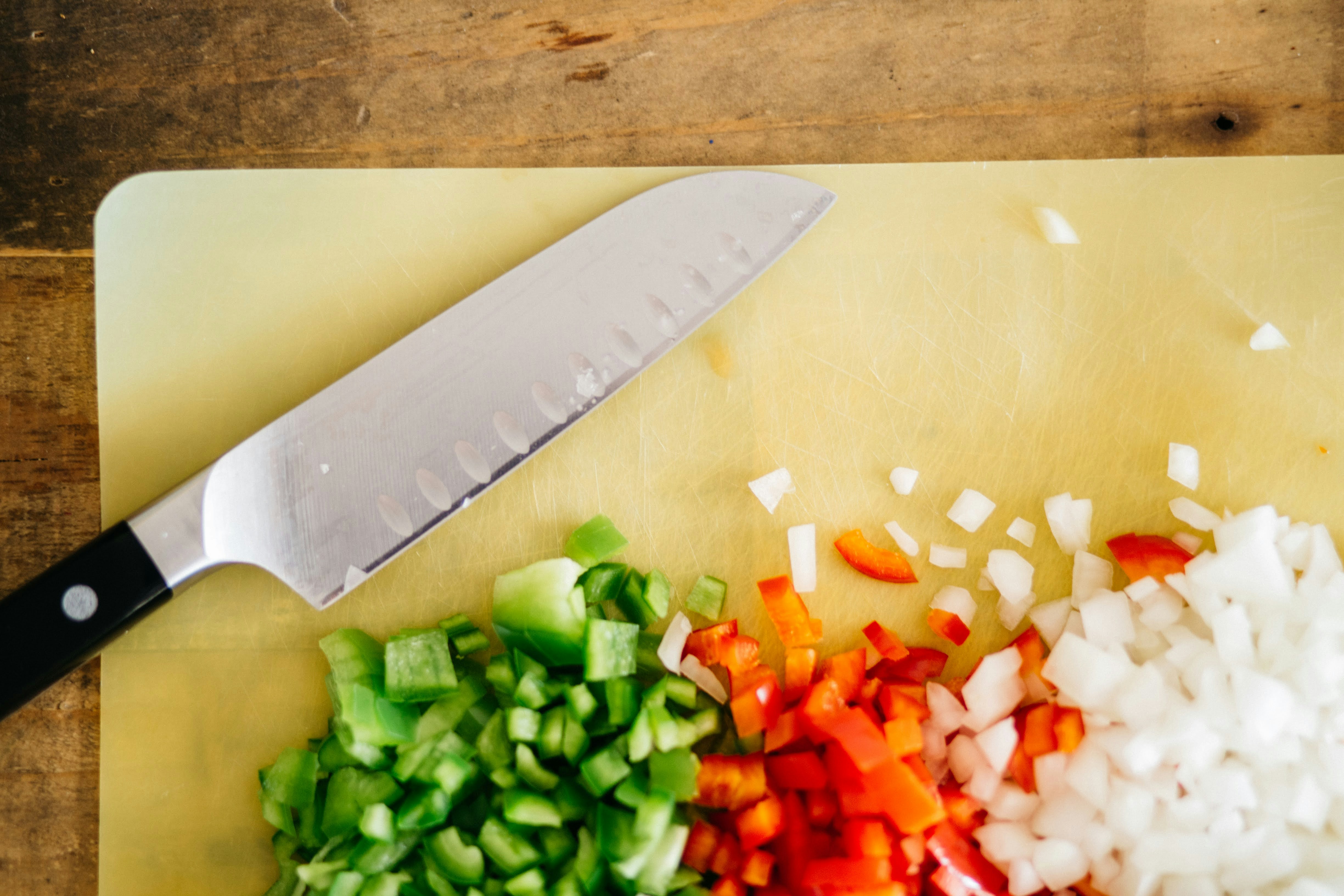 A knife chopping vegetables on a durable foldable plastic cutting board, showing no signs of deep scarring.