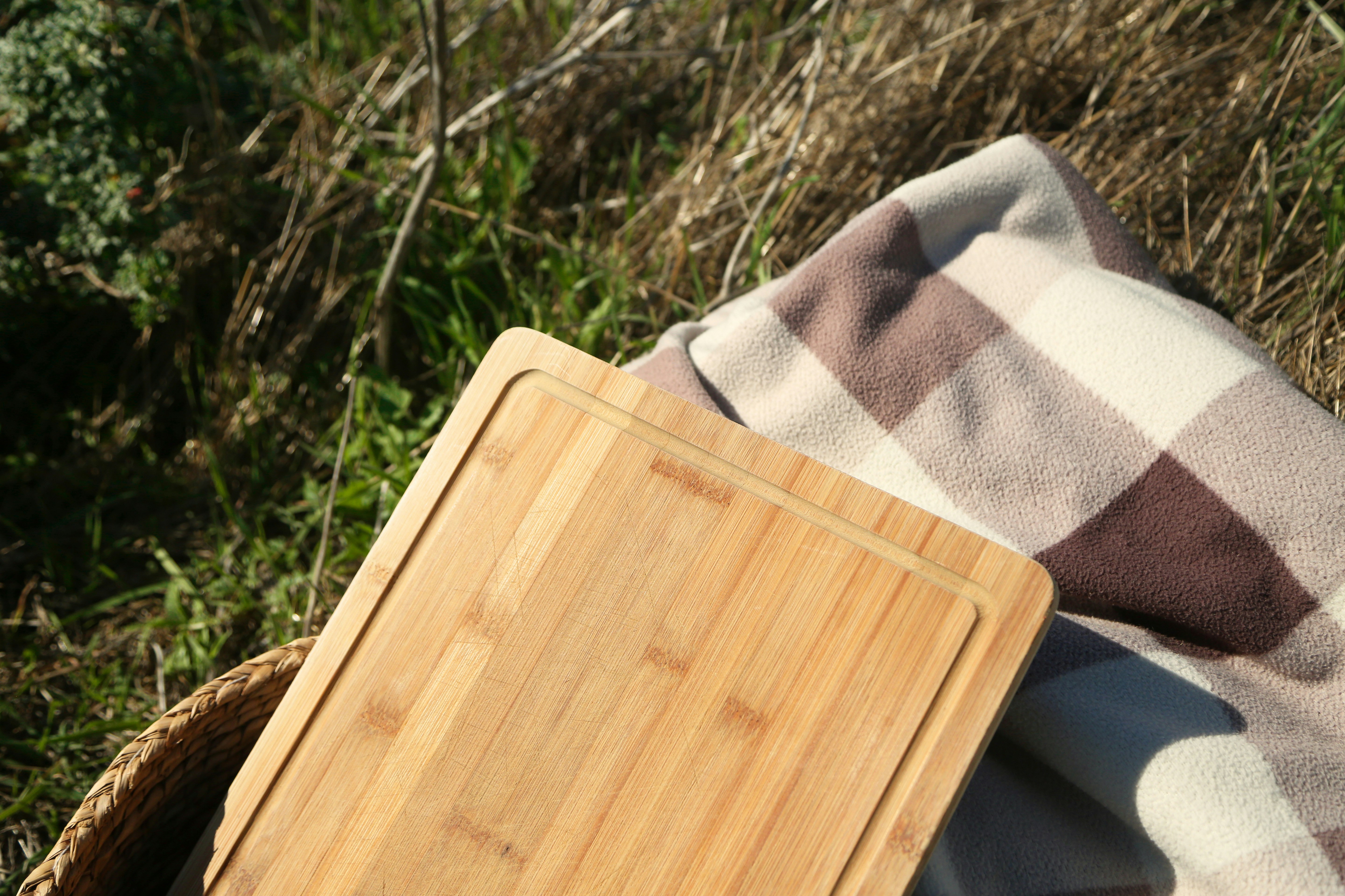 A person packing a lightweight, folded plastic cutting board into a picnic basket.