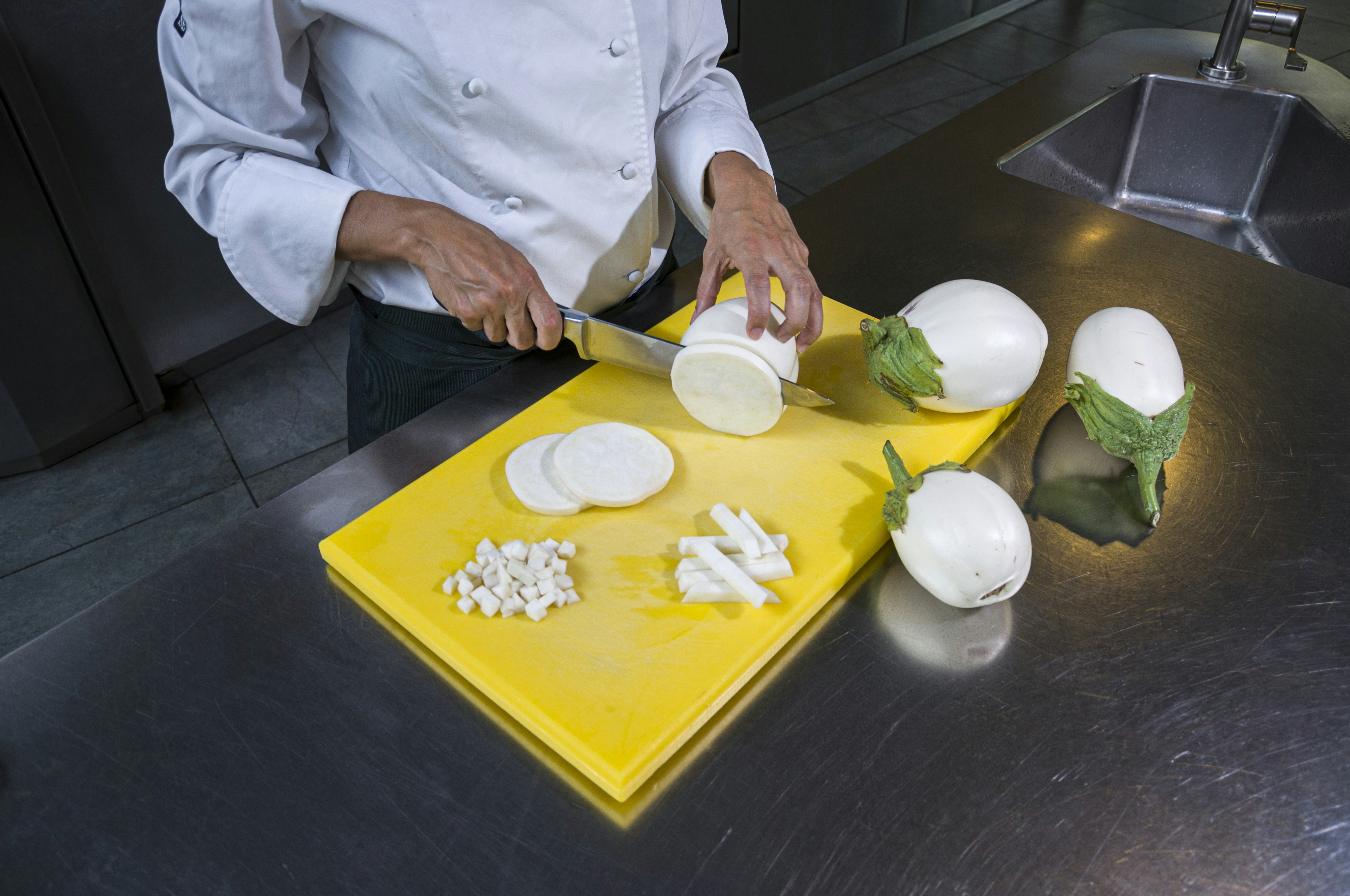 A chef chopping fresh vegetables on a white food-grade plastic cutting board.