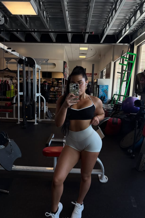 Woman in black white sports bra and gym shorts taking mirror selfie