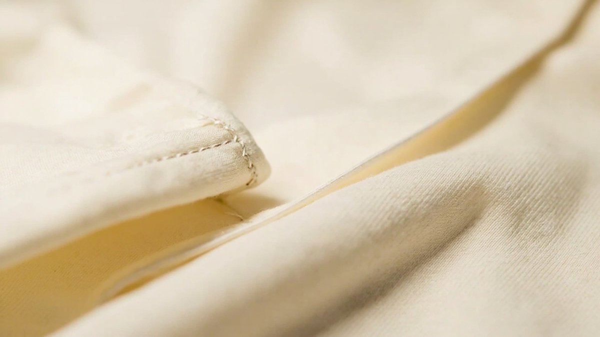 Close-up macro shot of premium short sleeve cotton T-shirt fabric texture showing tight-knit ring-spun cotton fibers, double-needle stitching on hem and sleeve cuffs, reinforced shoulder seams, demonstrating the high-quality construction expected from OEM manufacturing