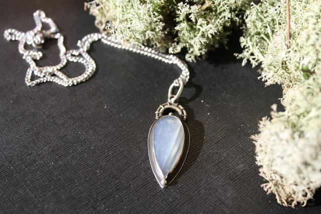 Silver necklace with a teardrop pendant on a dark surface
