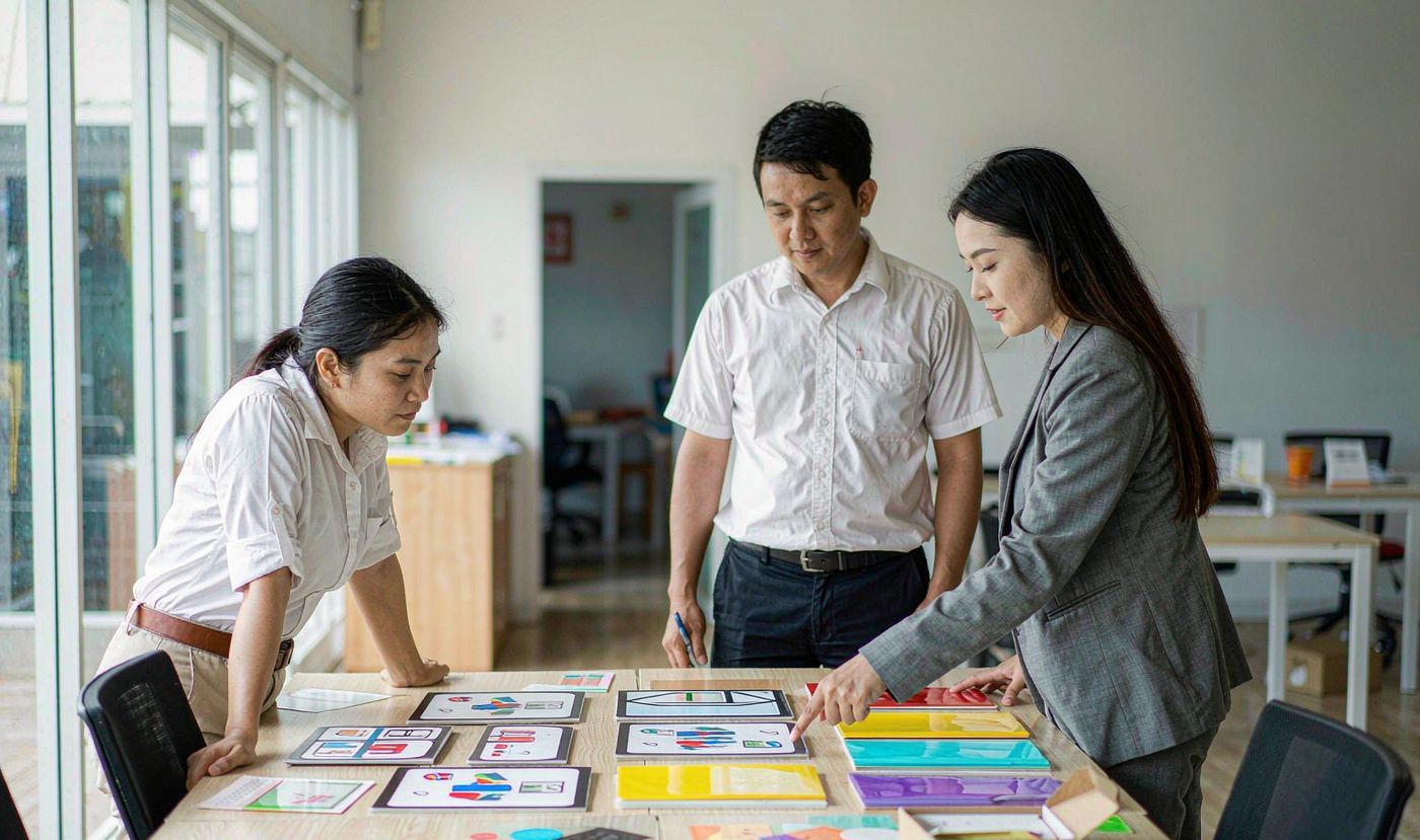 A design engineer, a project manager and a purchasing manager reviewing custom membrane switch sample panels together at a meeting table