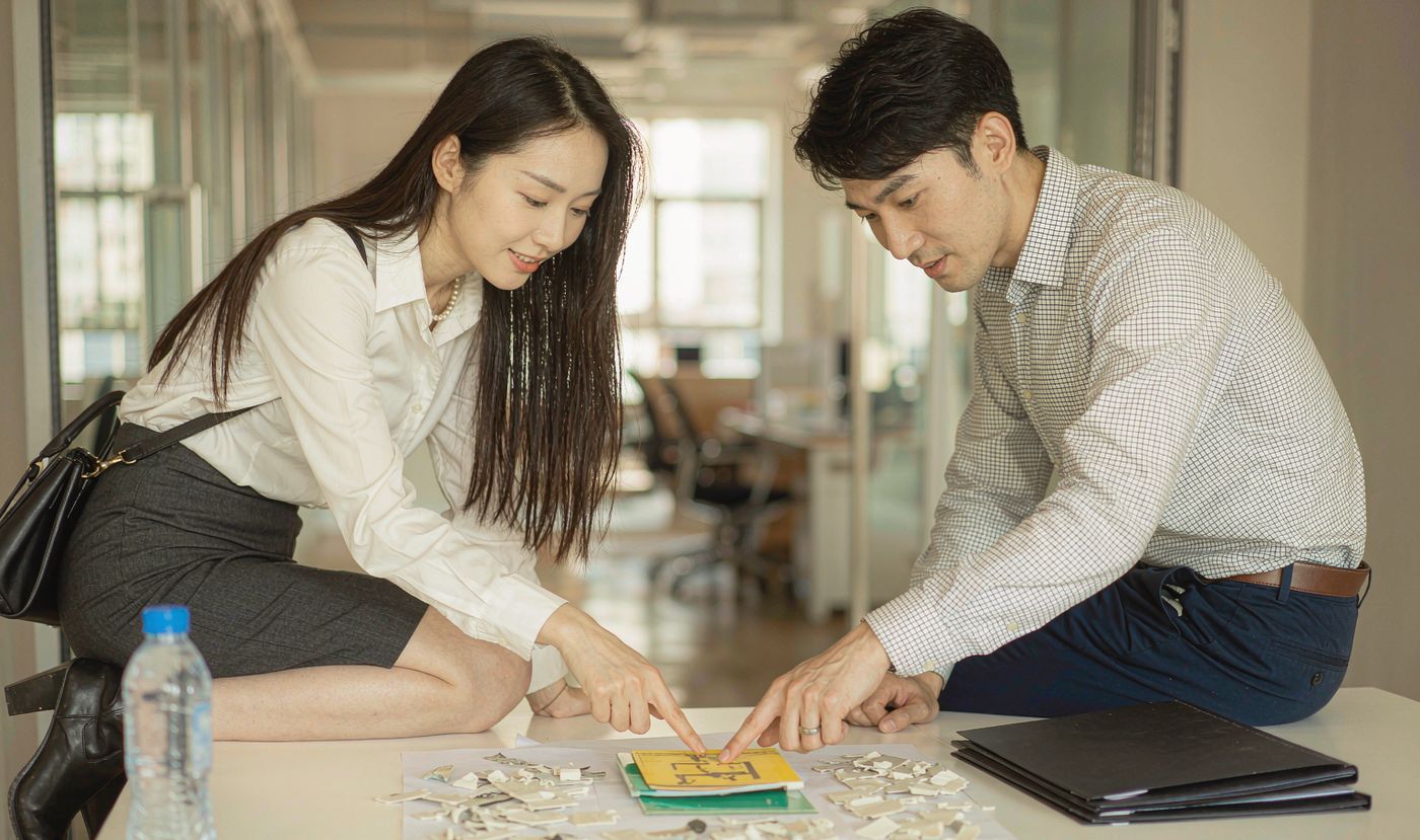 A procurement manager and a supplier sales engineer reviewing membrane switch sample parts together across a desk