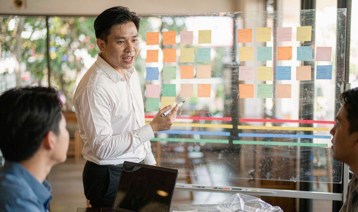 A project manager walking colleagues through the programme schedule on a planning board covered with milestone notes