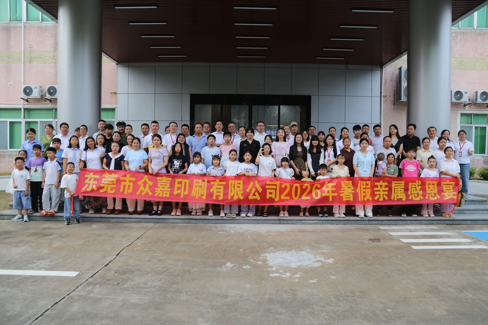 KeypadOne employees and their families hold the 2026 summer family appreciation banner and pose for a large group photo outside the company facility before departing for the banquet.