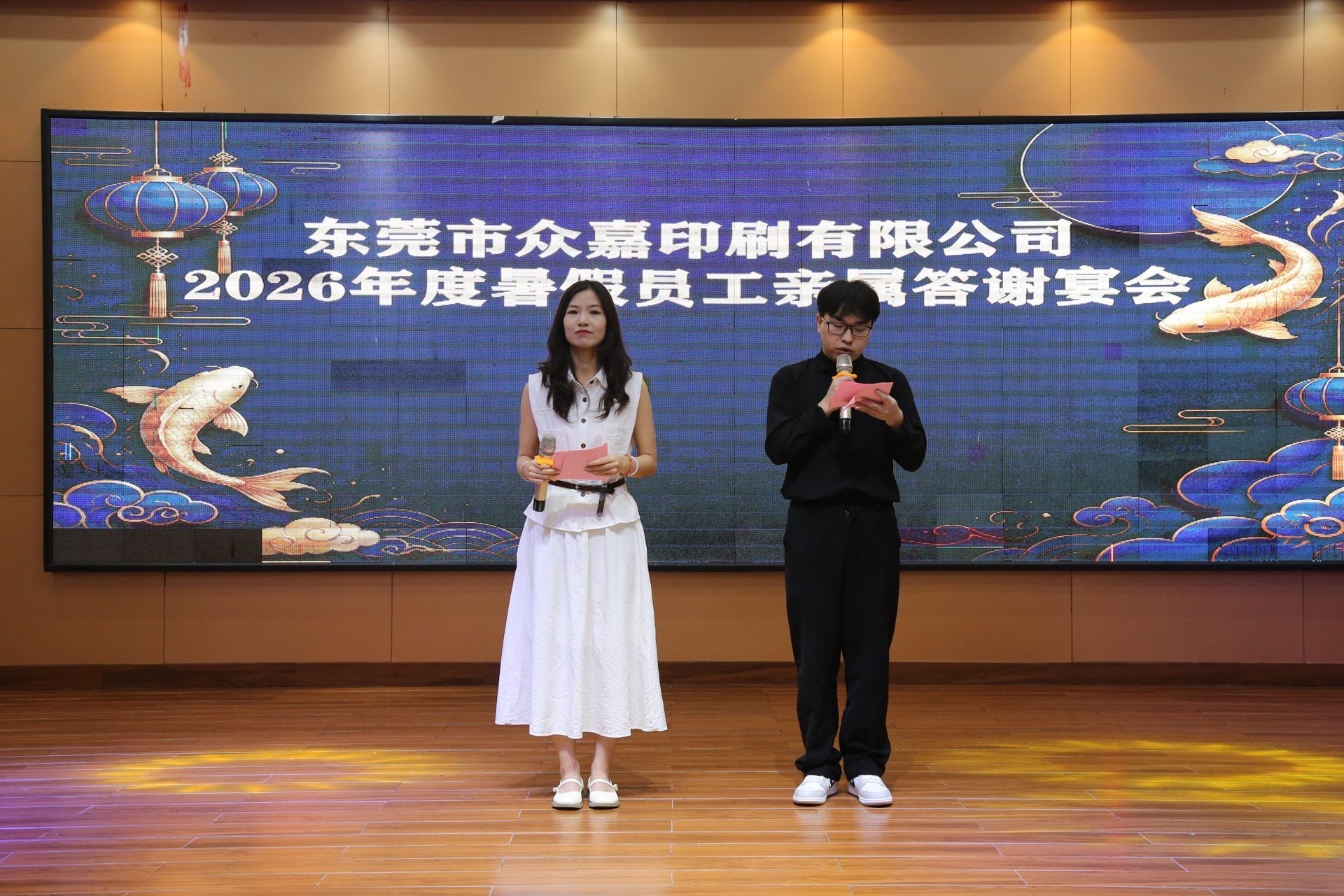Event hosts deliver the opening speech on stage in front of the 2026 family appreciation banquet backdrop.