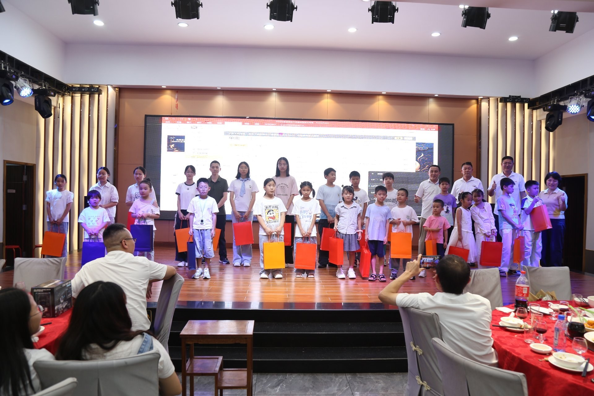 Children of KeypadOne employees stand on stage holding colorful gift bags prepared by the company.