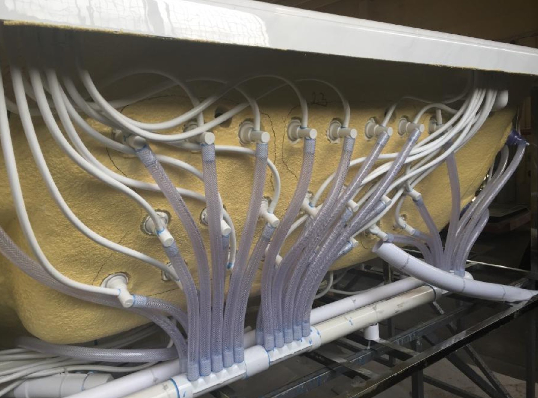 Jetted bathtub underside with braided water tubes and air lines at EEH factory