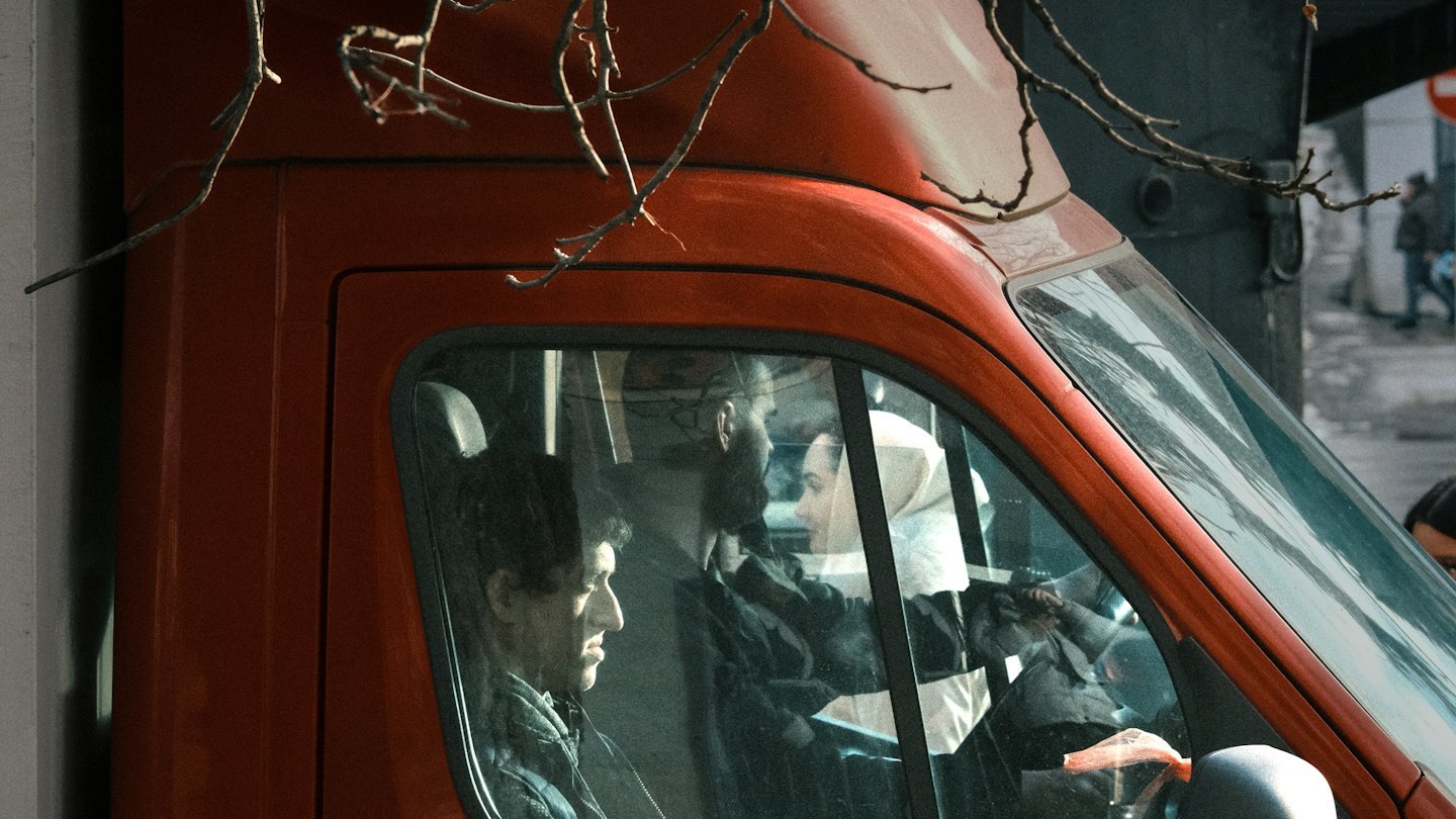 Driver and passenger seated in a red delivery vehicle