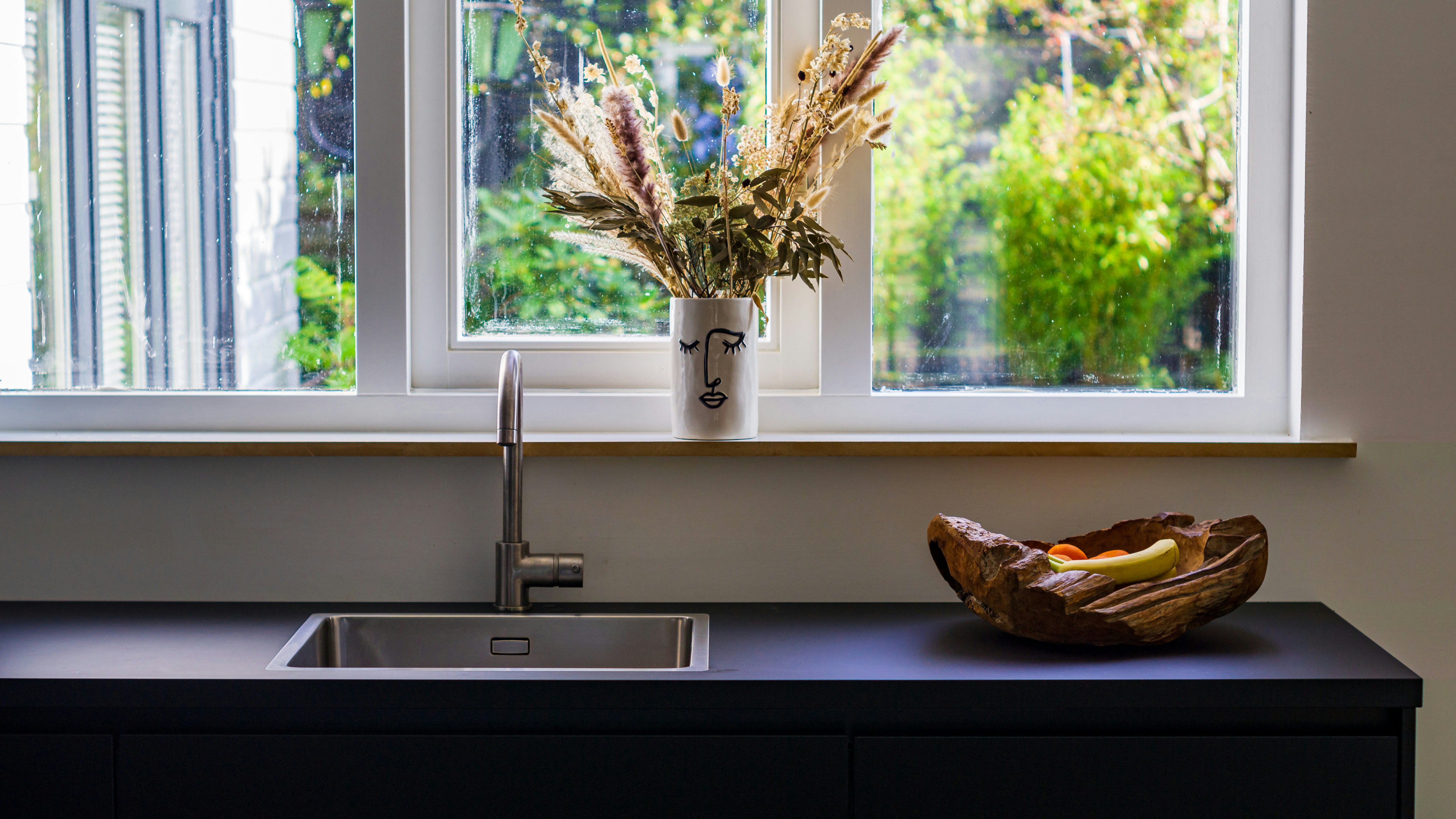 LEED and BREEAM sustainable stainless steel sinks A modern kitchen with a stainless steel sink, set against a backdrop of green plants, symbolizing sustainability.