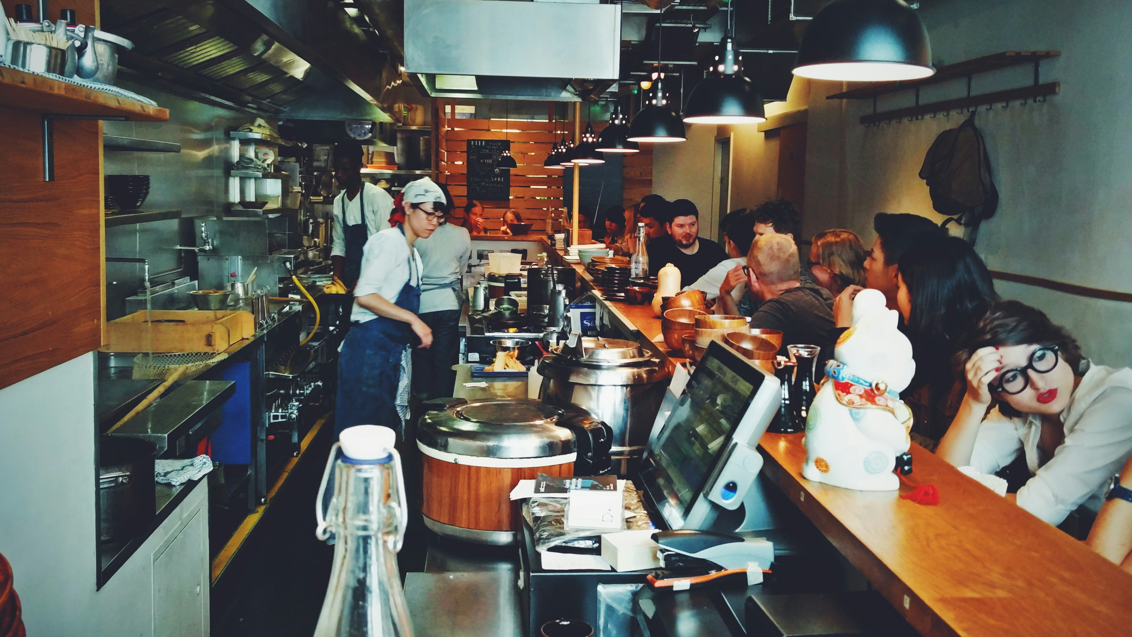 A busy commercial kitchen showing various stainless steel stations, including sinks and racks