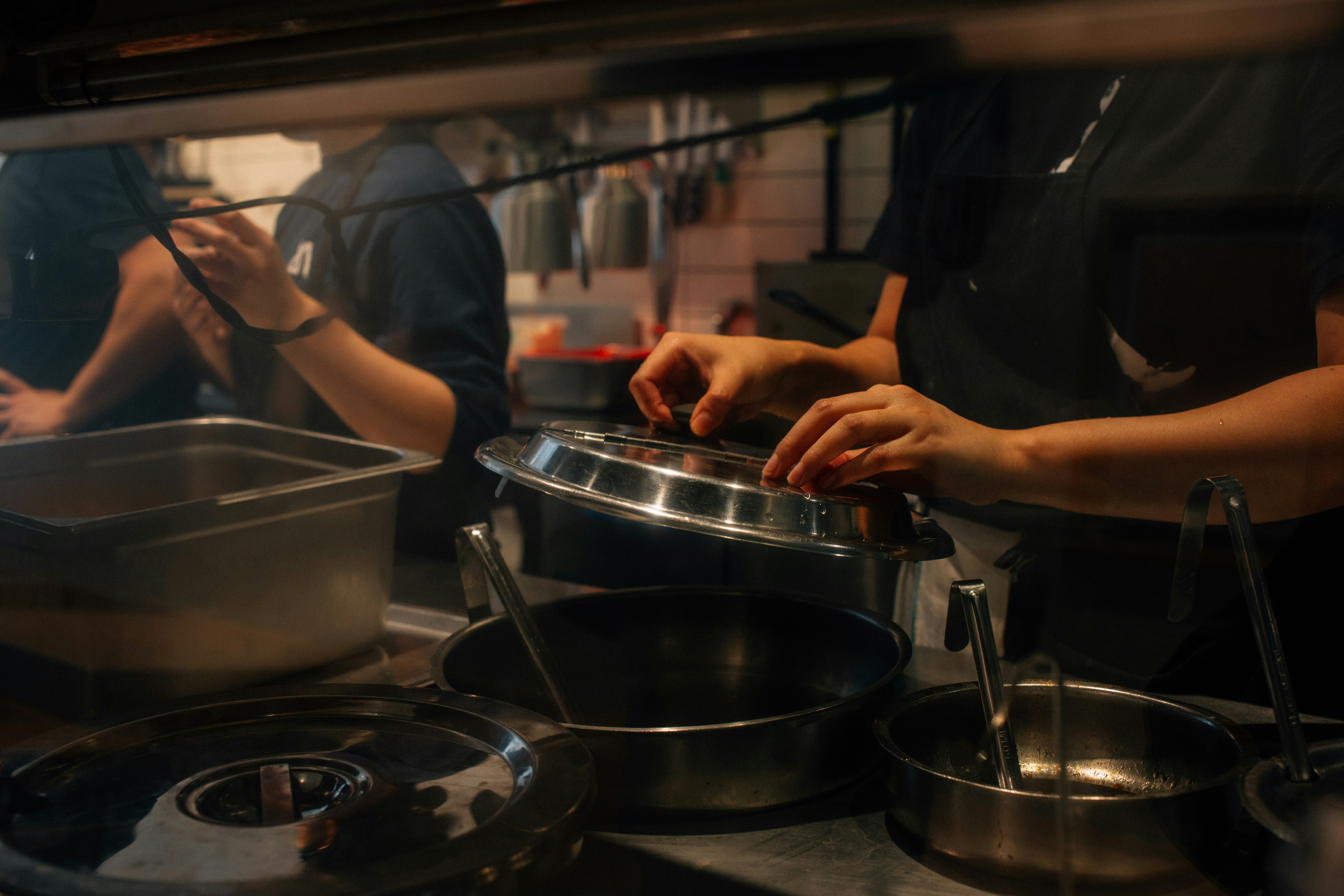 A busy restaurant kitchen with chefs washing their hands at a dedicated stainless steel sink.