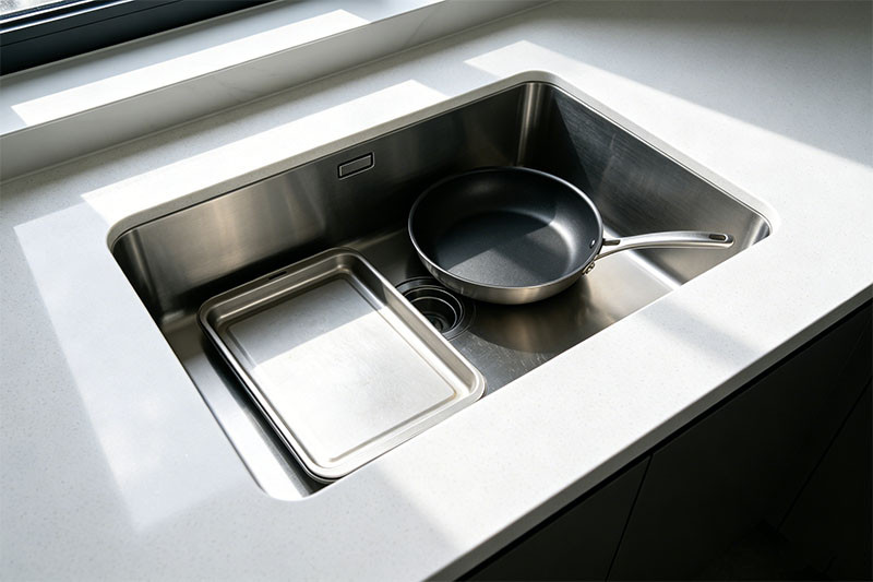 A large, stainless steel single basin self-rimming sink filled with soapy water and a large pot.