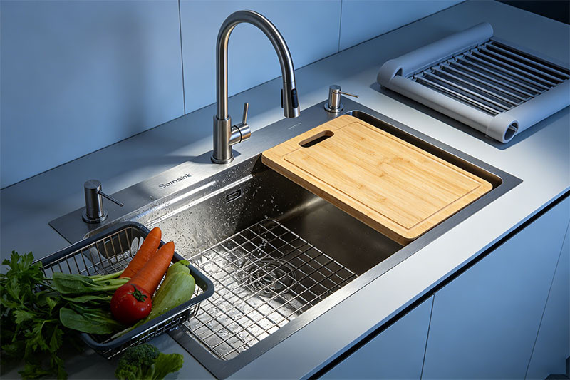 A stainless steel workstation sink with an integrated cutting board, colander, and roll-up drying rack in use.