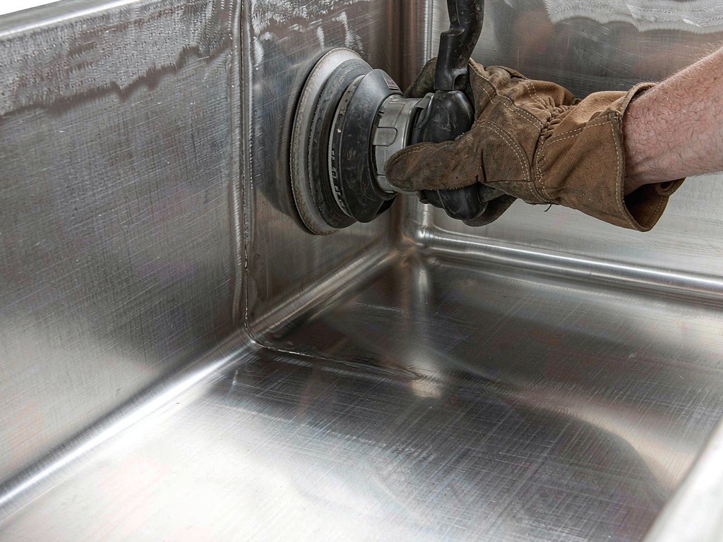 Craftsman polishing a brushed stainless steel sink surface in a factory workshop