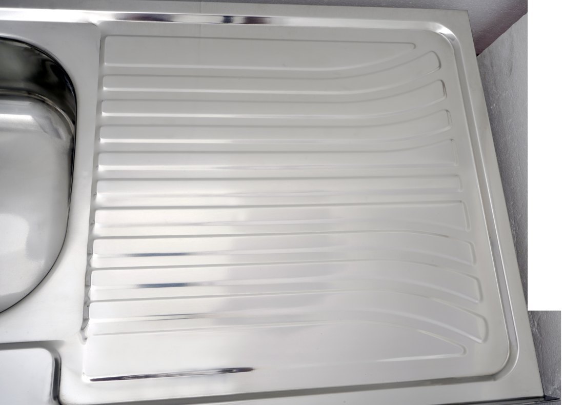 Grooved drainboard surface of the stainless steel sink with pressed channels that carry runoff back towards the bowl