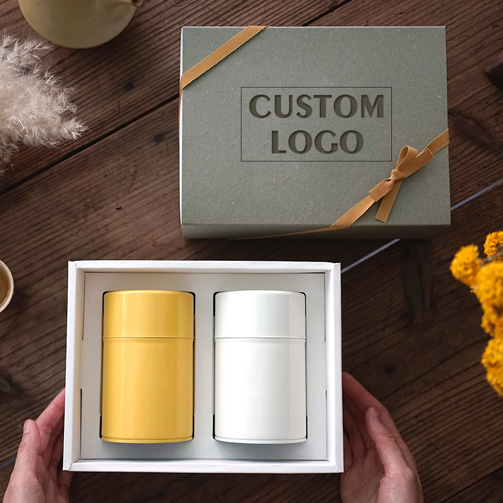 Luxury tea gift box with ribbon and two fitted cylindrical tea tins in yellow and white