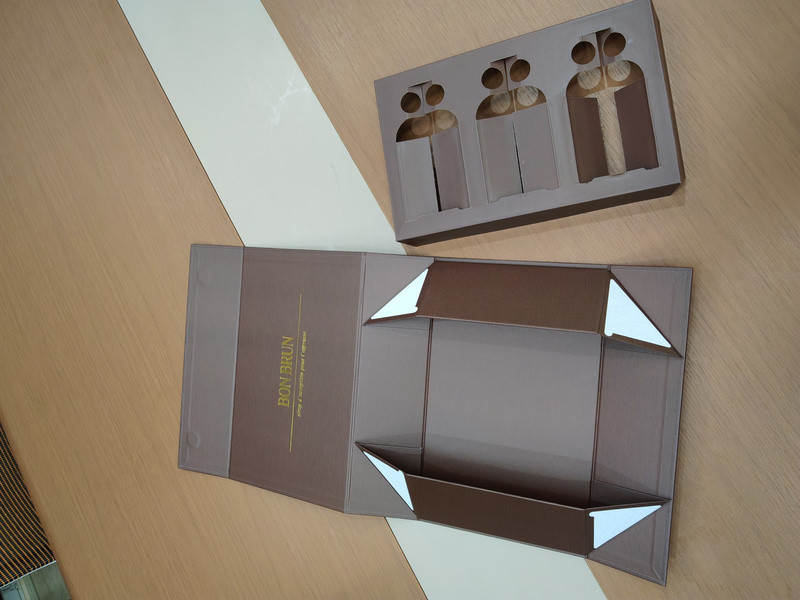 Foldable magnetic liquor gift box structure laid flat beside a custom three-bottle die-cut paperboard insert