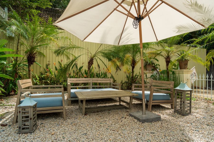 Cozy garden patio with wooden chairs, table and a patio umbrella surrounded by greenery