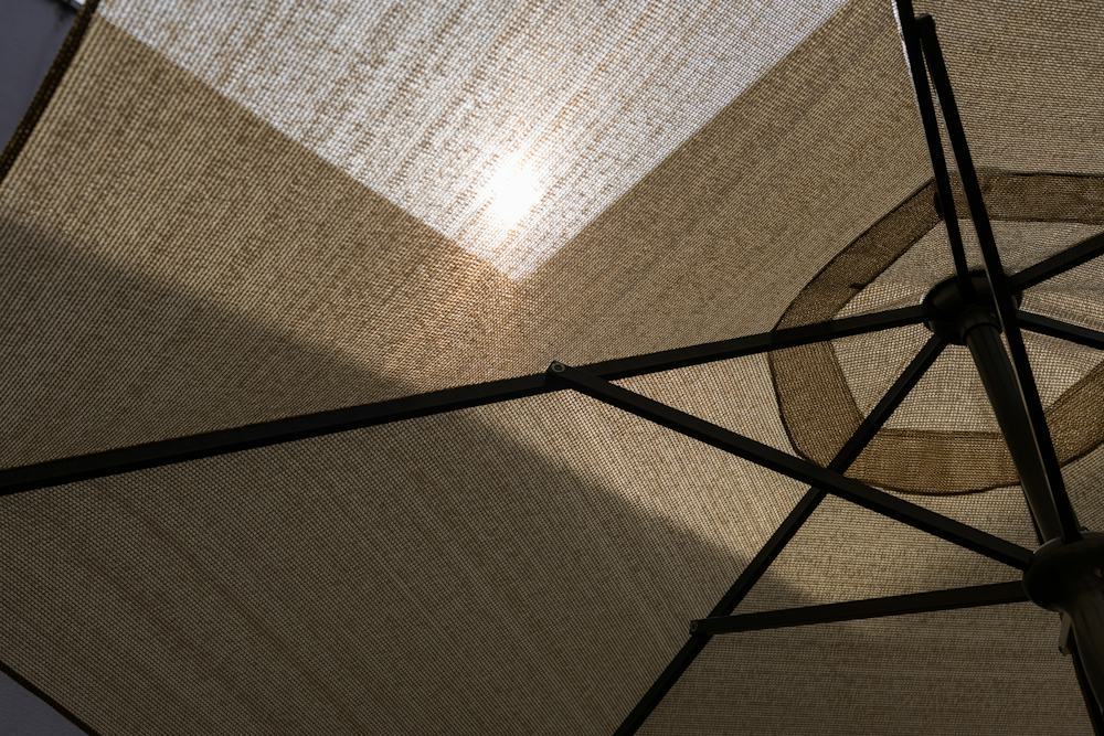 View from below an open umbrella canopy with sunlight filtering through the woven fabric