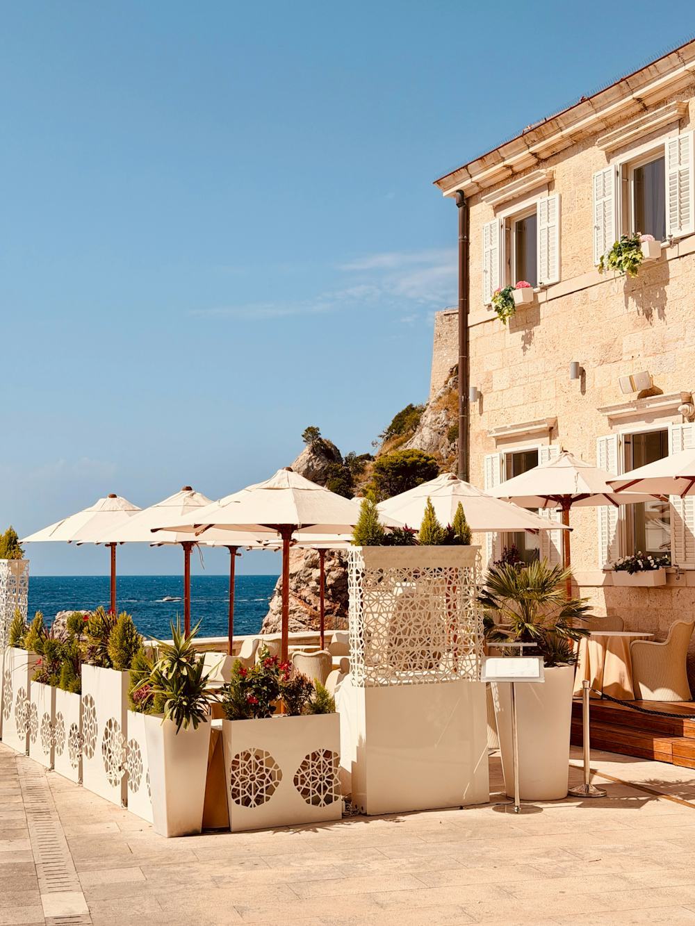 Seaside terrace with tables and chairs shaded by a row of cream umbrellas