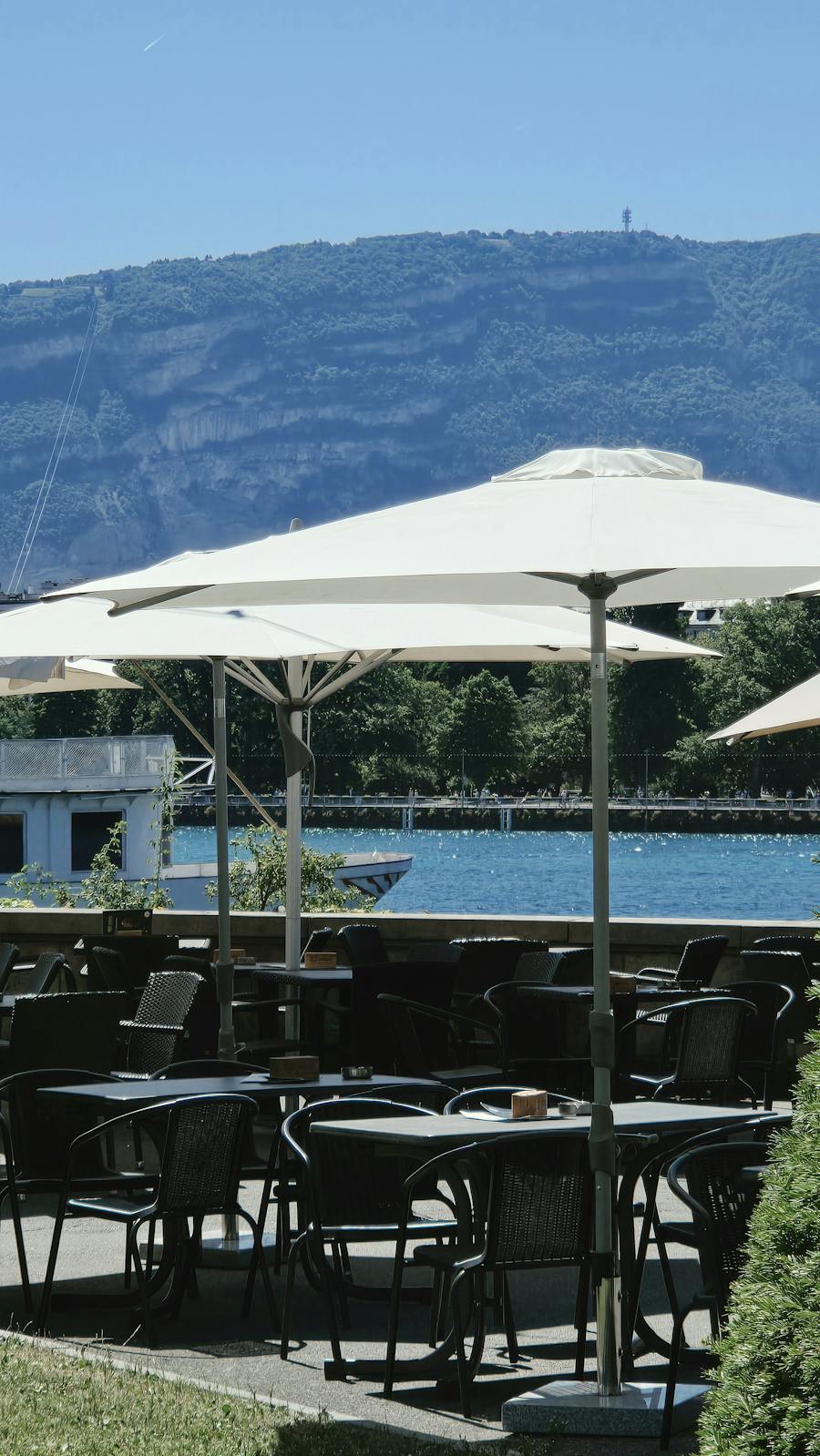 Lakeside terrace with cream umbrellas over tables and a base plate visible on the paving
