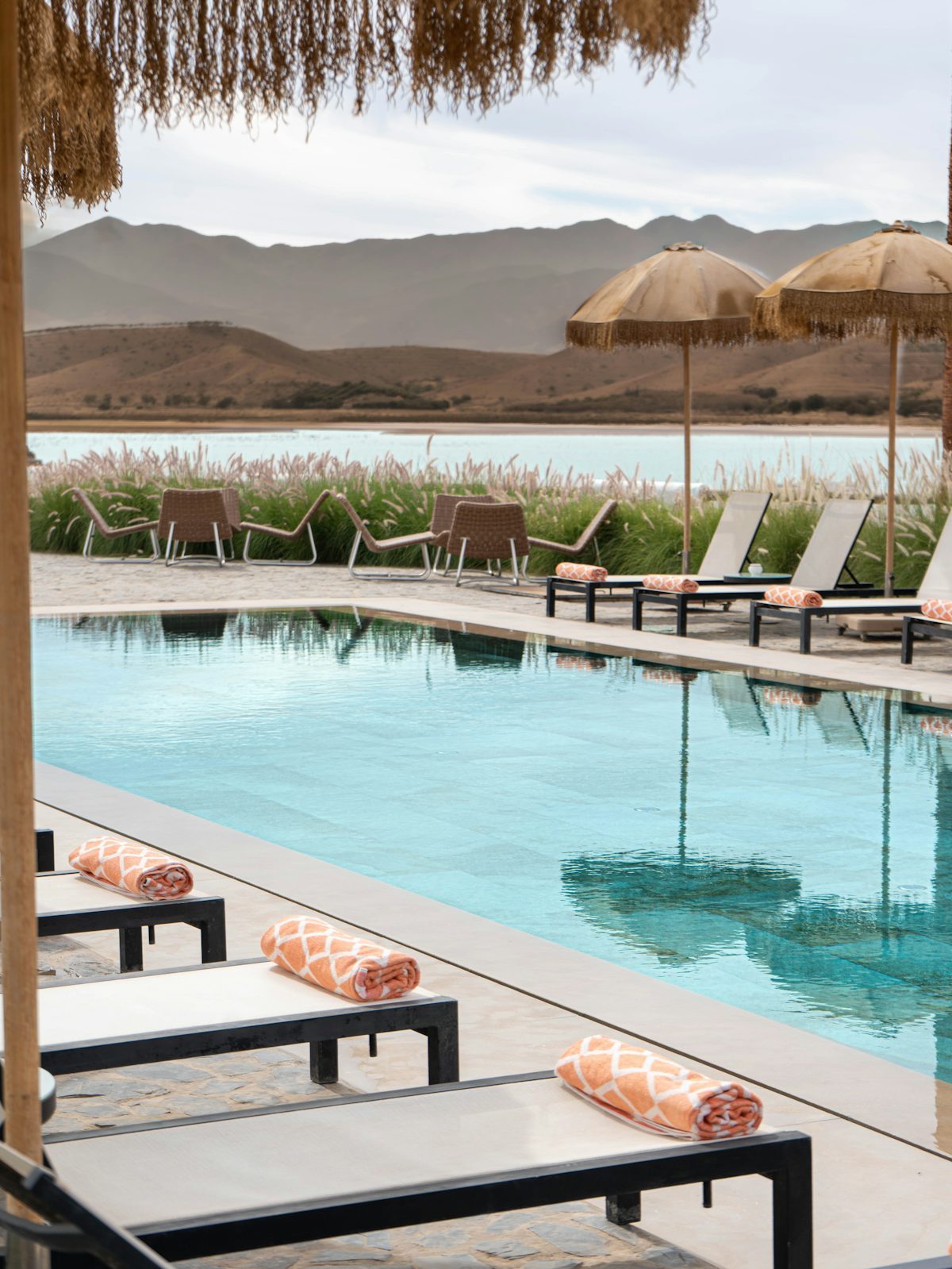 Resort poolside with freestanding parasols on stone paving beside loungers