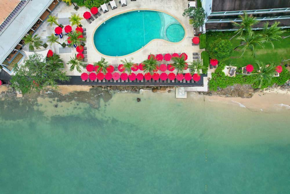 Aerial view of a clifftop resort with rows of umbrellas above a beach and turquoise sea