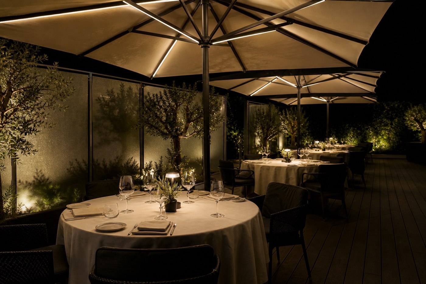 Restaurant terrace at night with lights glowing along the ribs of the umbrellas over set tables