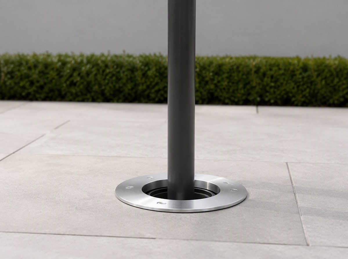 Flush brushed steel in-ground umbrella socket set into pale paving with the pole rising from it