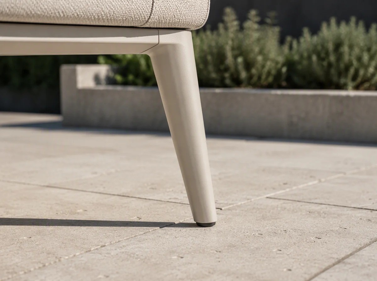 Close view of a cream powder-coated tapered aluminium leg meeting pale stone paving