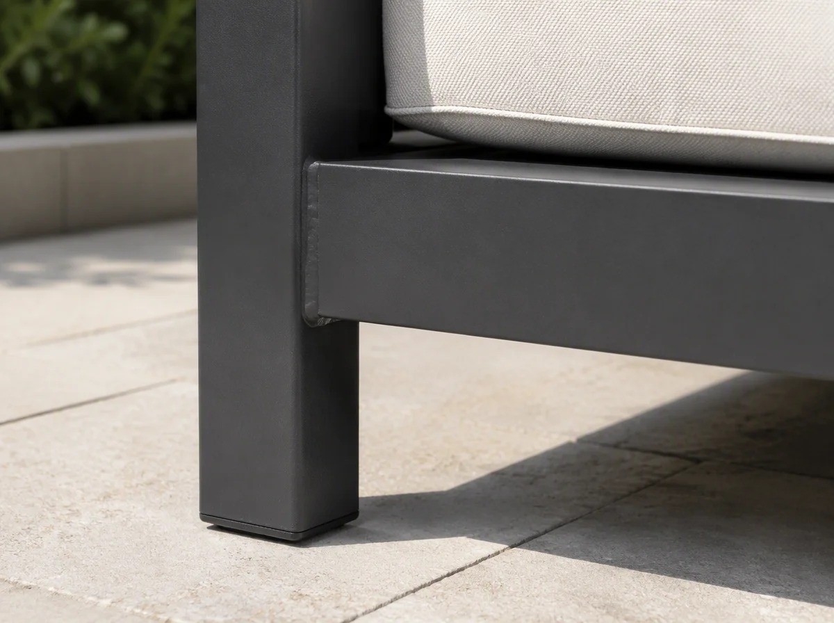 Close view of the welded corner and foot of a matt charcoal aluminium outdoor sofa frame on pale stone paving