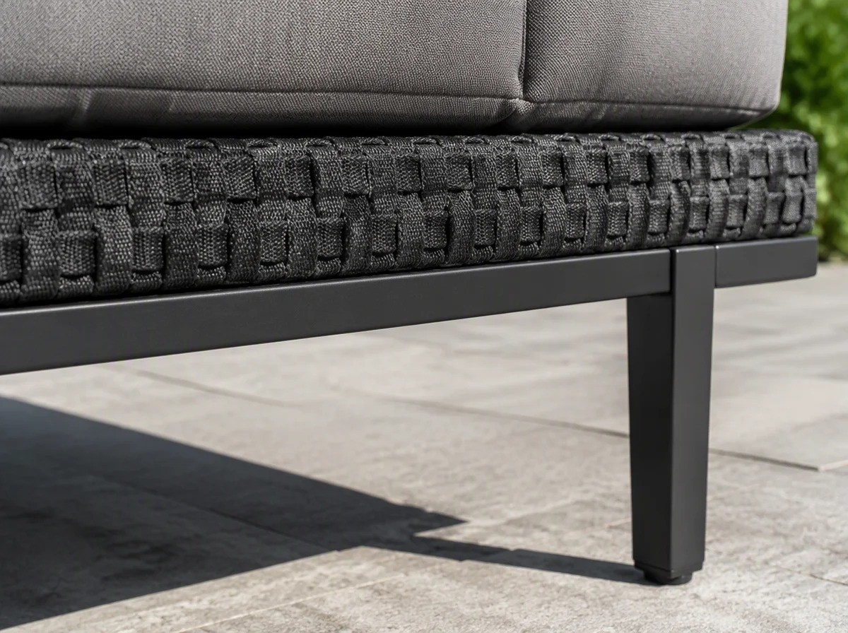 Close view of a band of woven strap webbing running along the charcoal seat rail of an outdoor sofa