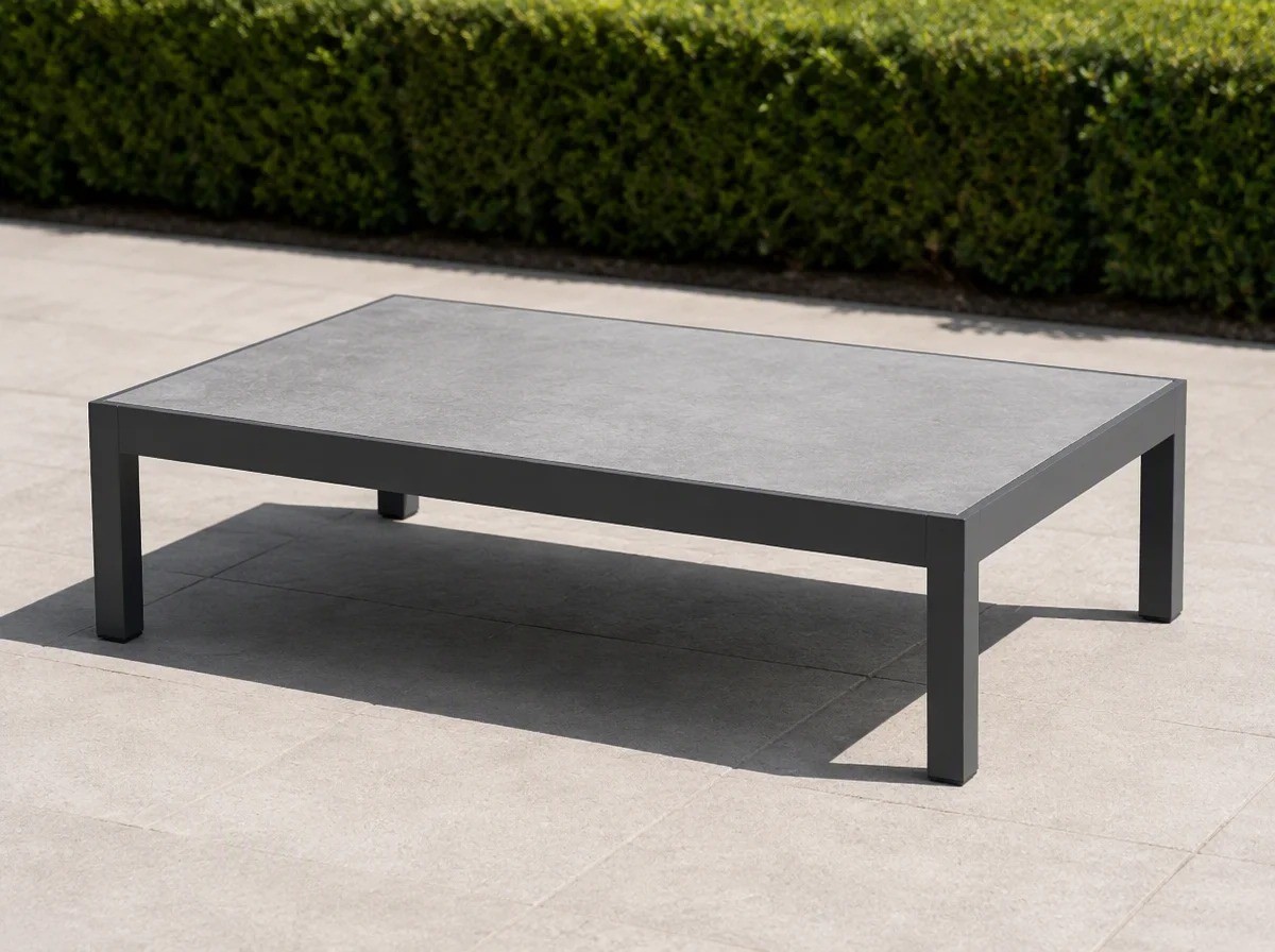 Low rectangular outdoor coffee table with a charcoal frame and a pale grey slab top on stone paving