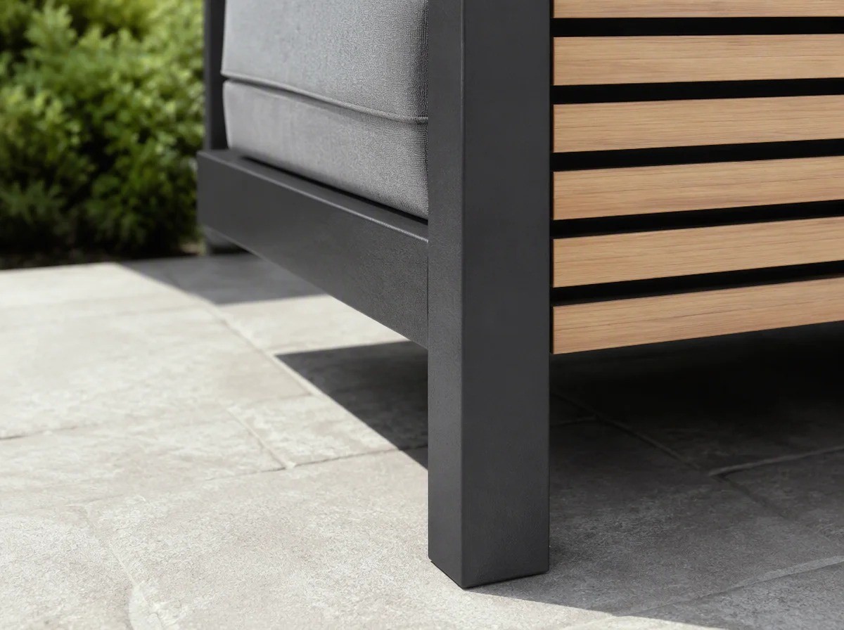 Close view of a charcoal aluminium outdoor sofa frame corner with the slatted side panel and a leg on stone paving