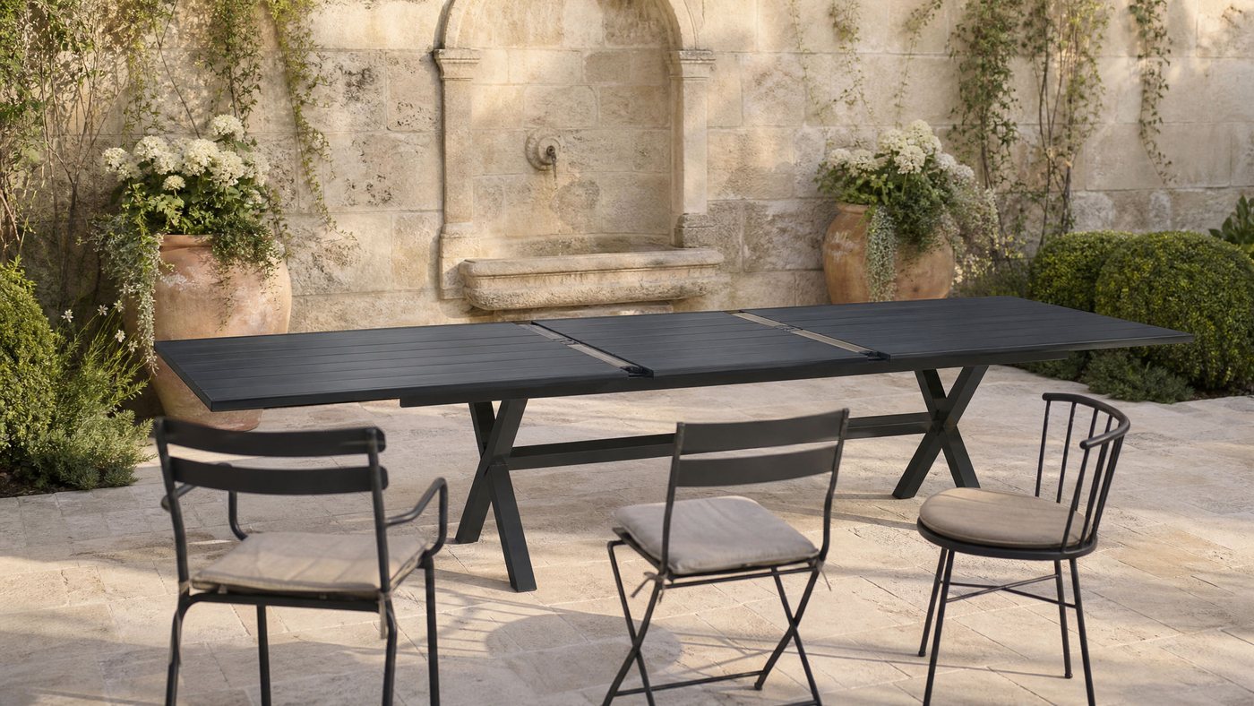 Extendable aluminium dining table on a stone courtyard with a wall fountain