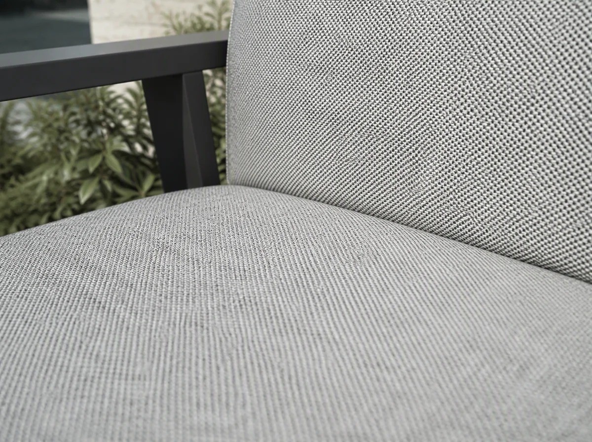 Close view of the light grey outdoor upholstery fabric on the seat of a dining armchair showing its dense speckled woven texture