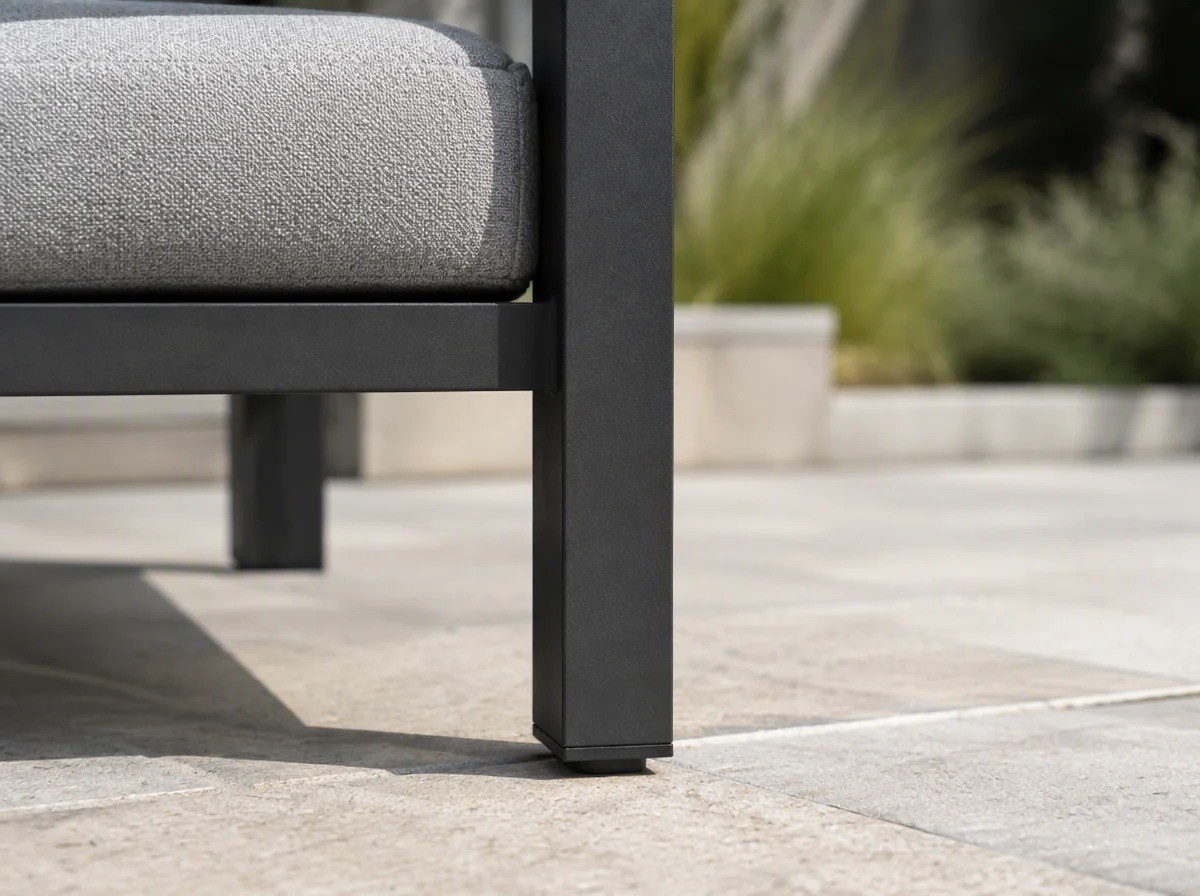 Close view of the charcoal steel front leg of an outdoor dining armchair meeting pale stone paving