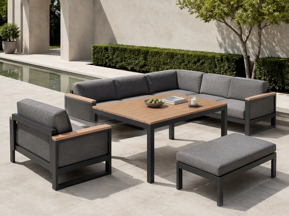 Six-piece charcoal aluminium corner sofa set with solid teak armrests and grey cushions grouped around a low half-height table beside a reflecting water channel