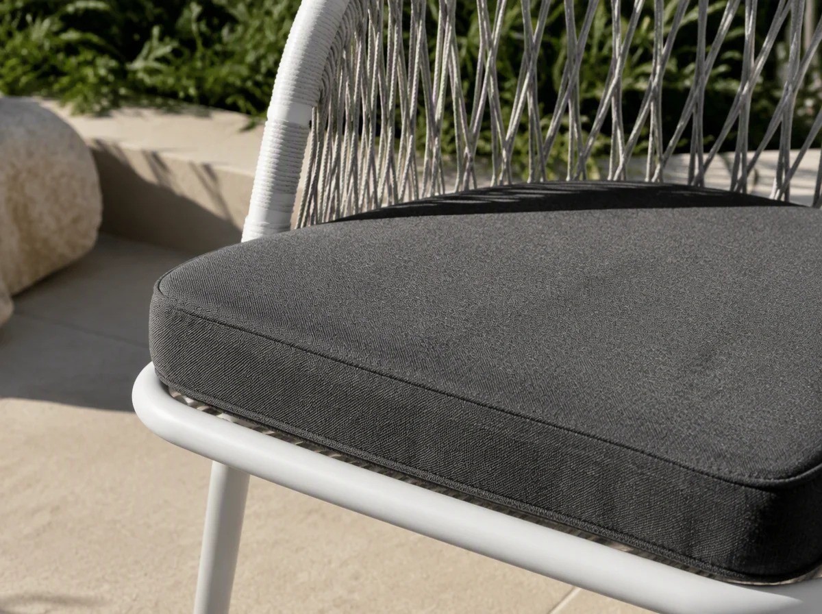 Close view of a thick dark grey loose seat cushion resting on the white frame of a rope-weave chair