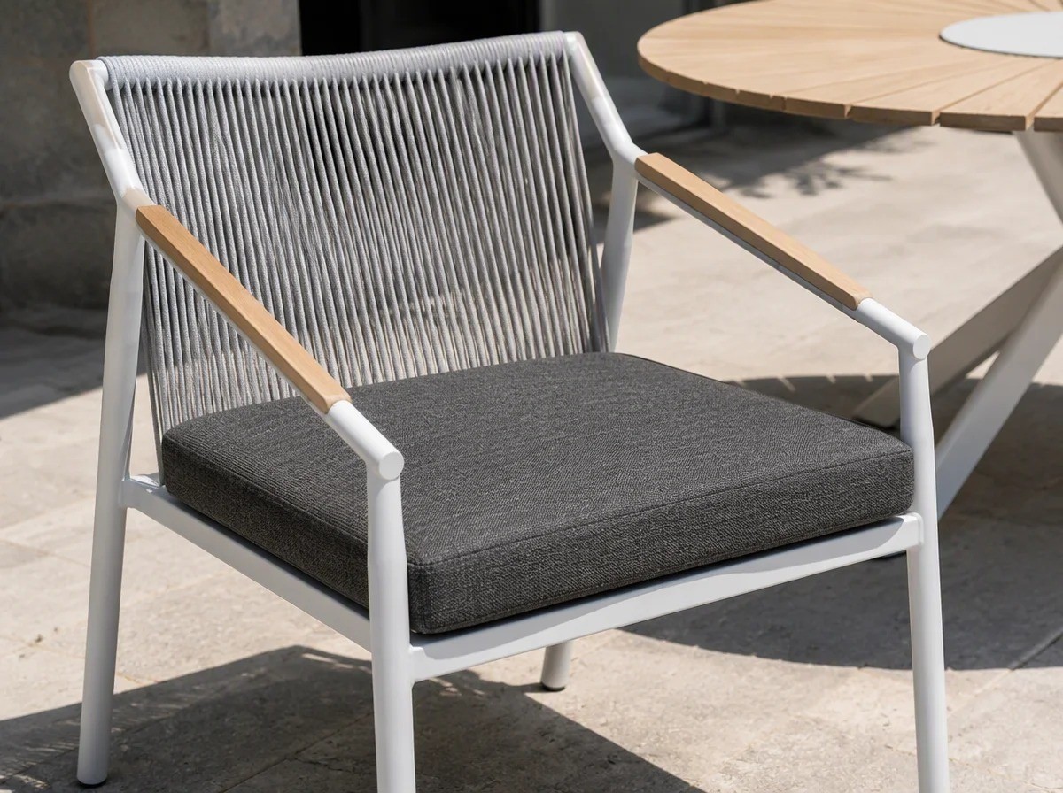 Close view of a thick dark grey loose seat cushion resting on the white frame of a rope-back chair