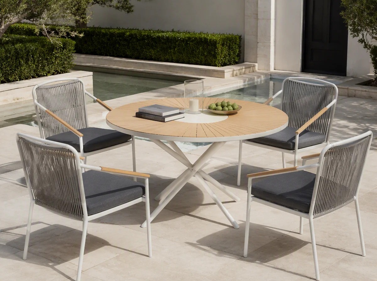 Round pale wheat sunburst-slat outdoor table on a central cross base with four rope-back chairs in a villa courtyard