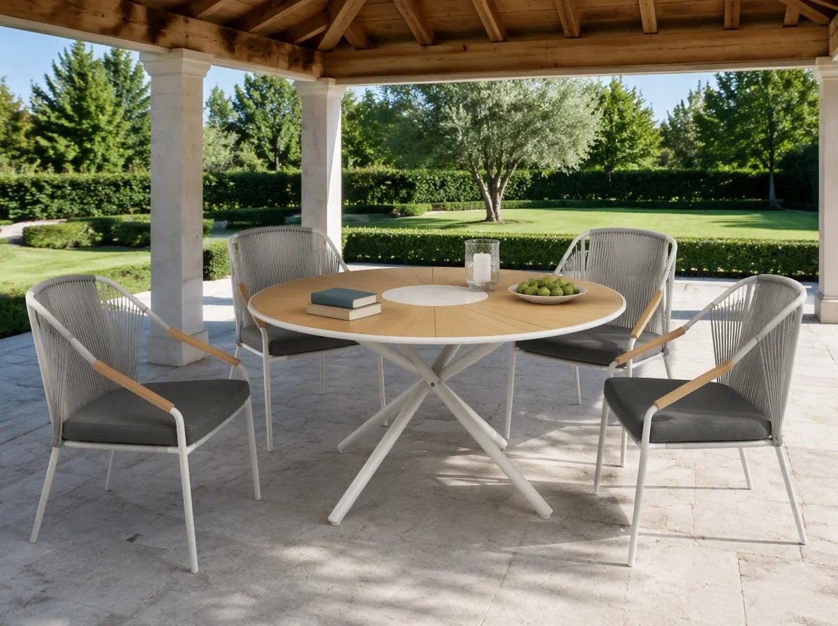 Round sunburst-slat outdoor dining table with a central cross base and four rope-back chairs under a covered garden pavilion