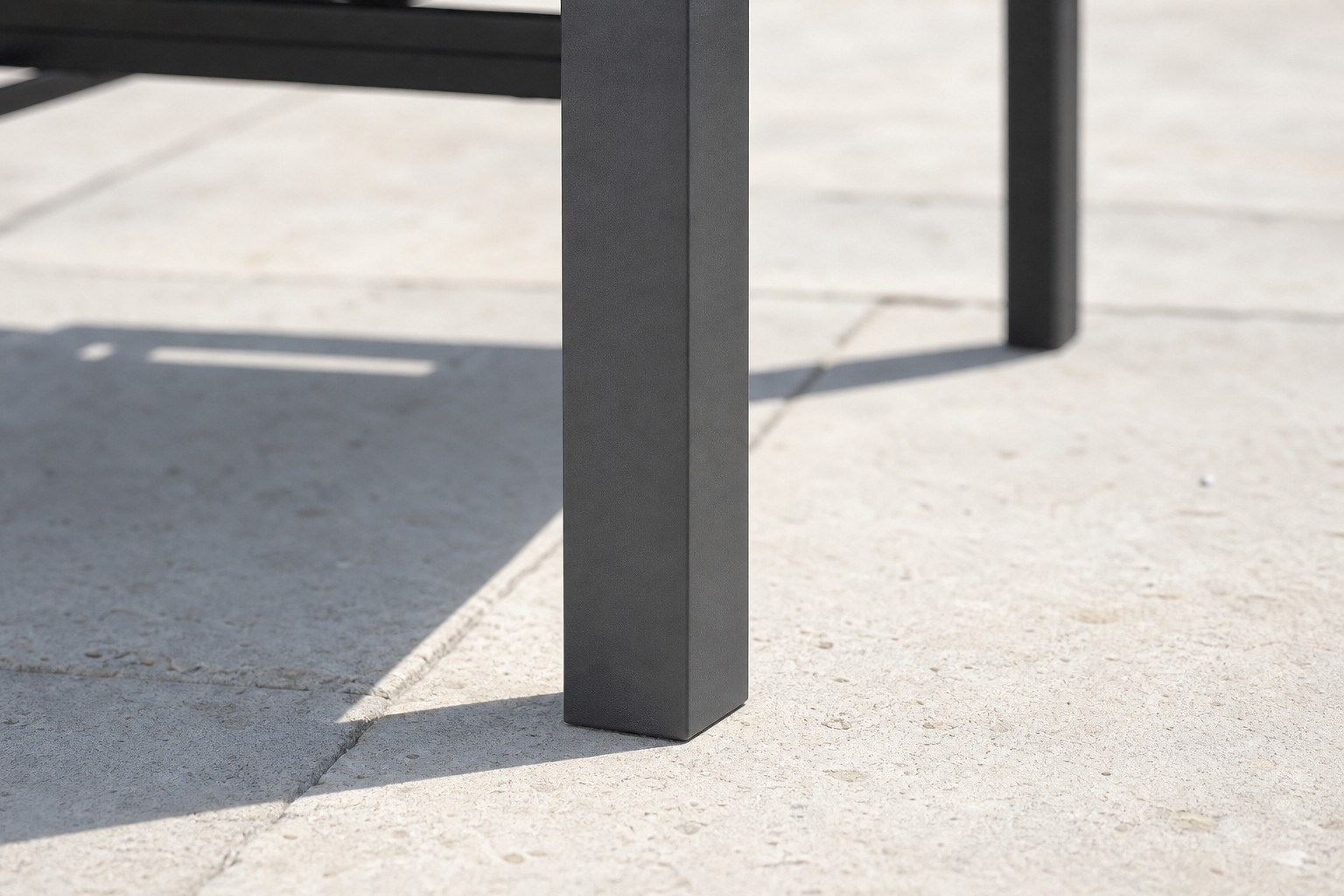 Close view of the square-section leg of the garden armchair meeting the paving, with its cast shadow