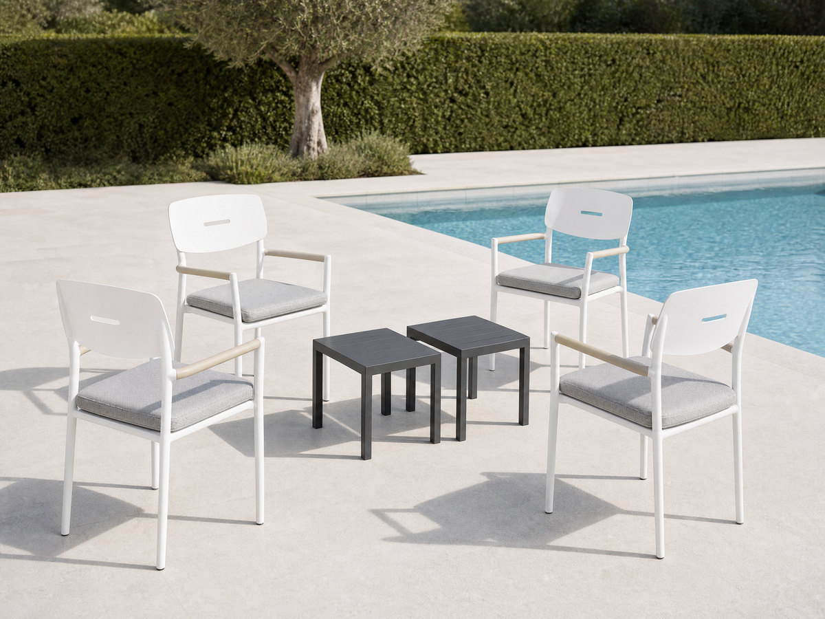 Hotel pool deck with identical white aluminium armchairs set around small charcoal side tables beside calm blue water